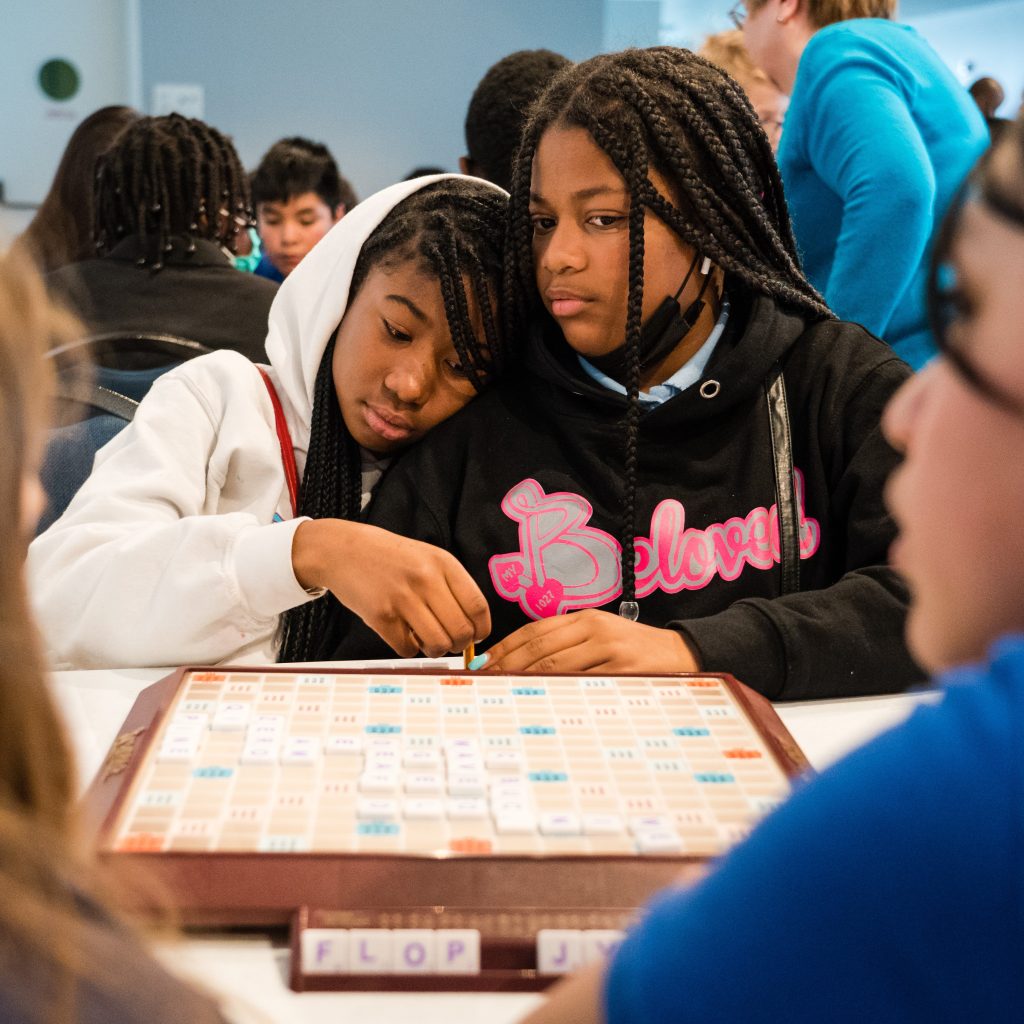 Two friends feel safe; leaning on one another during scrabble 